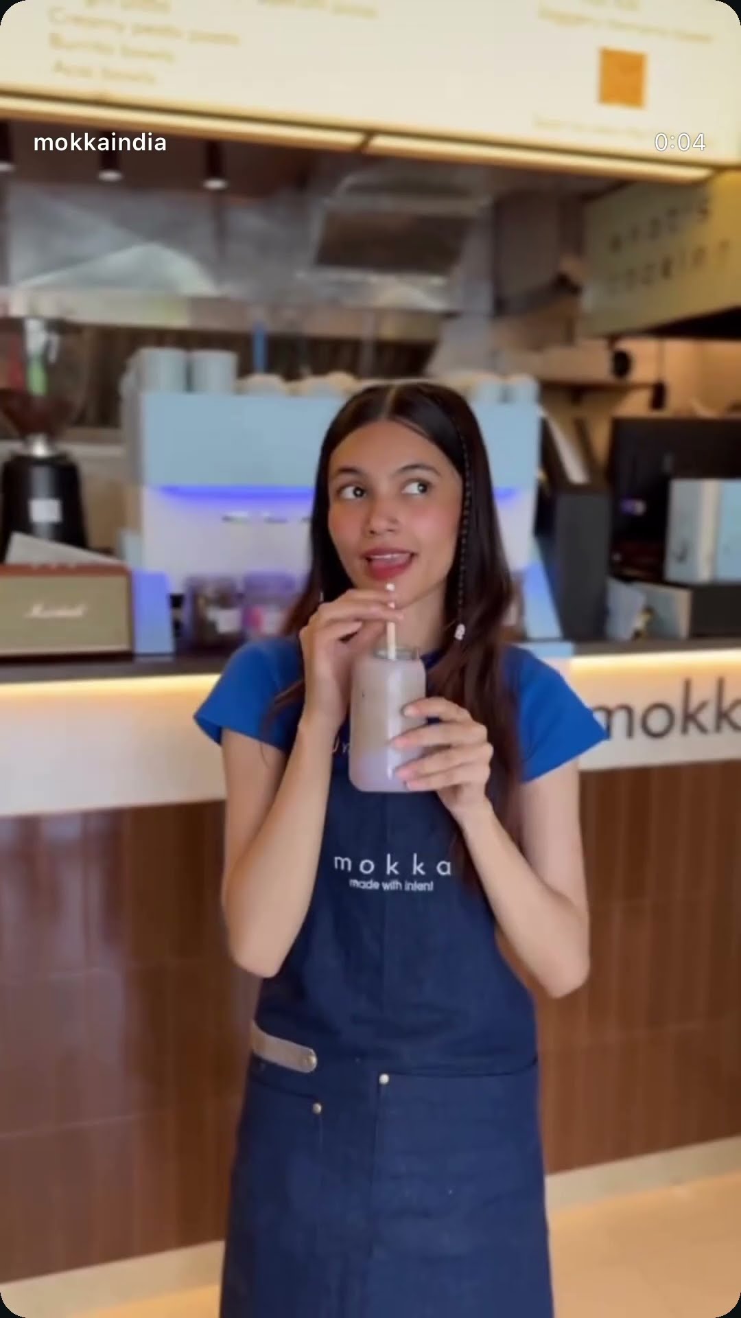 A barista in a Mokka apron drinking an iced coffee